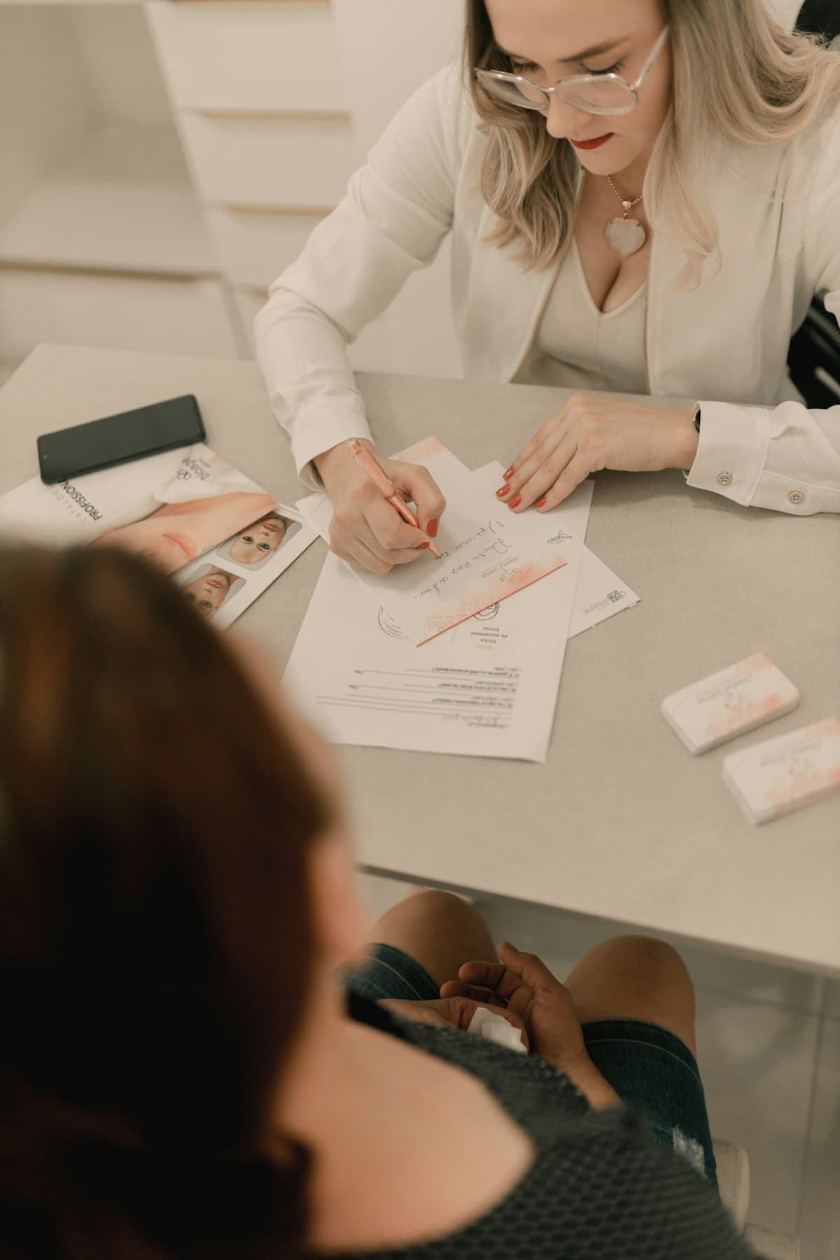 An aesthetic clinic consultant writing a treatment plan across the table from a client.