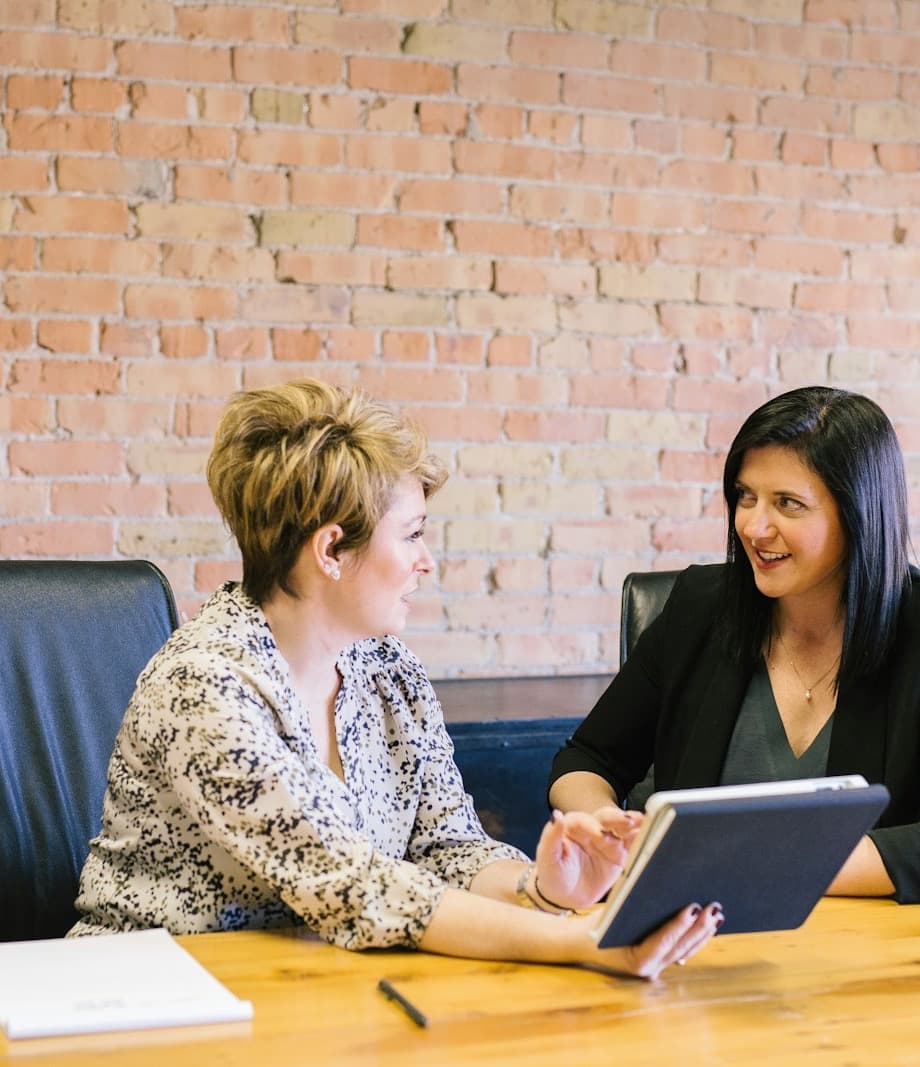 A marketing strategist reviews a growth plan on a tablet with a practice owner at a wooden table.